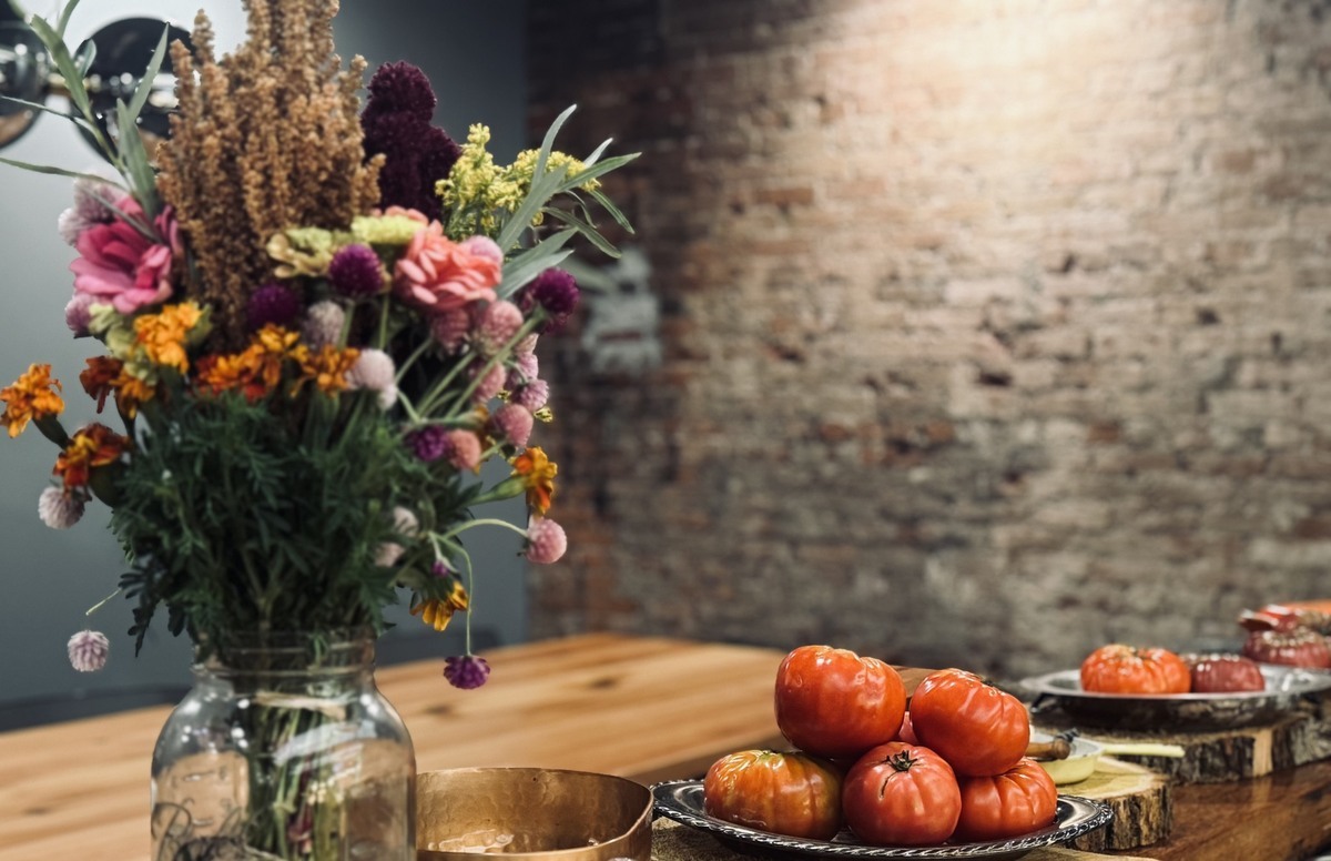 a vase of flowers sitting on a wood tabletop next to a plate of fresh tomatoes