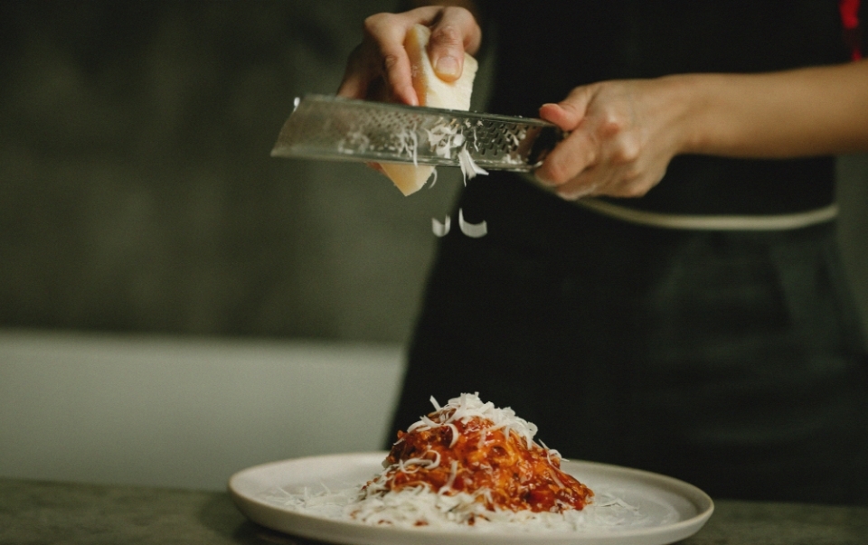 Waiter shredding parmesan over spaghetti.