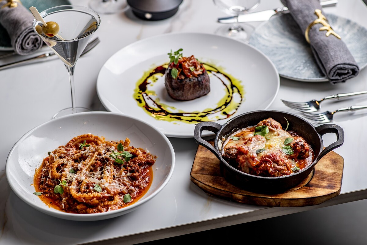 two full plates of food sitting on a wood tabletop next to a side of fresh bread and a glass of white wine